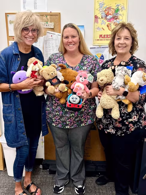 Personal de la División de Vehículos Motorizados de Colorado sonríe mientras sostiene animales de peluche.