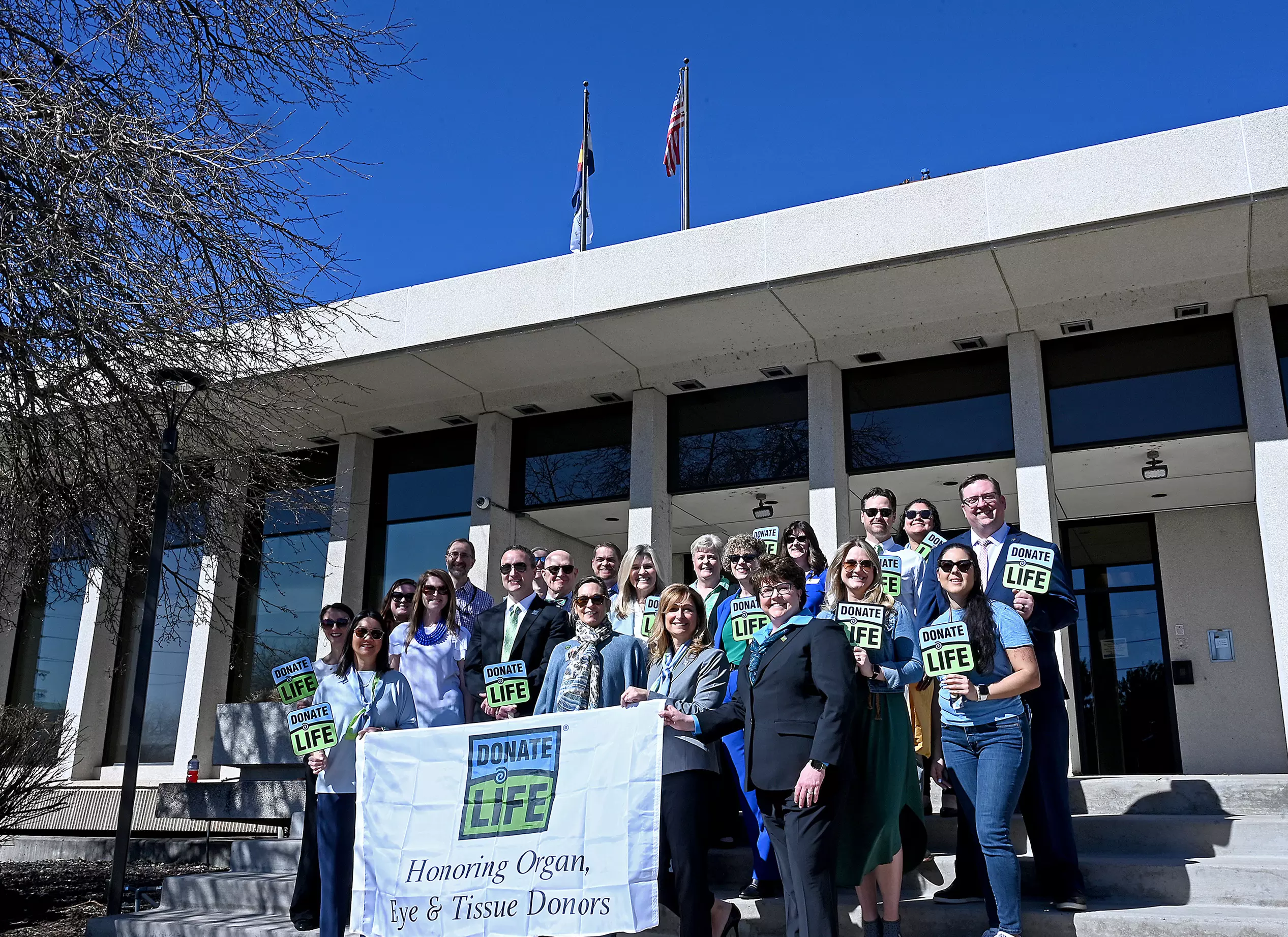 Members of the Colorado Department of Revenue, Division of Motor Vehicles and Donate Life Colorado pose for a photo Monday, April 10, 2023, as the Donate Life flag flies under the Colorado State flag overhead on the roof of CDOR’s main office in Lakewood. The Division of Motor Vehicles and Donate Life Colorado hosted a flag-raising ceremony to commemorate National Donate Life Month. This ceremony helped bring awareness of what it means to be an organ donor and highlights the partnership between Donate Life 