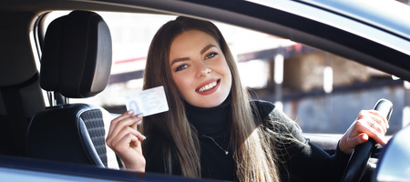 Young female driver sitting in car holding her license and smiling