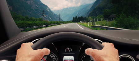 Driver view of hands on wheel and overlooking the dashboard while driving down the road through the mountains