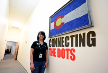 Pueblo Driver license employee stands in a hallway with a framed Colorado logo on wall and words Connecting the Dots under frame.