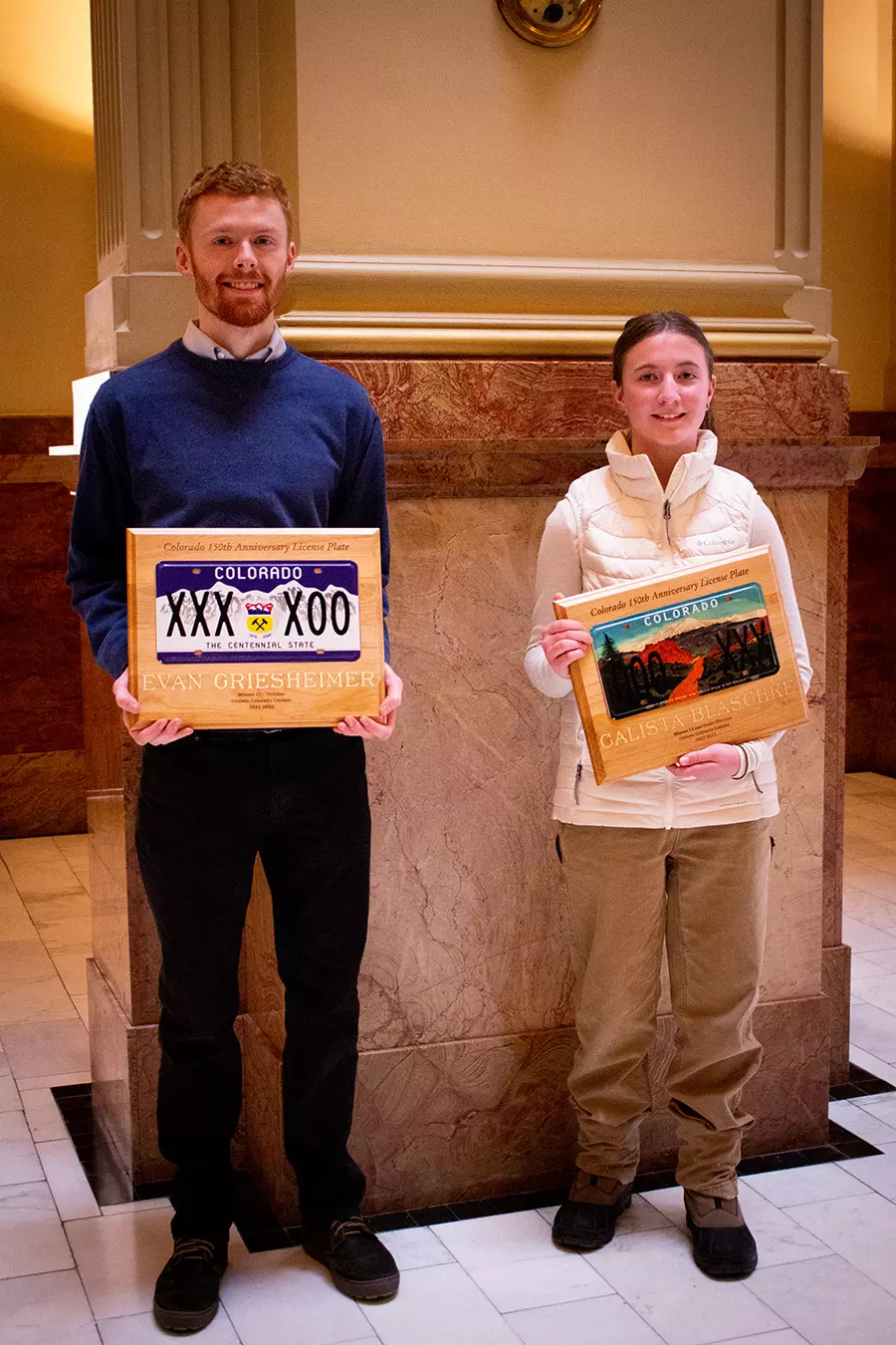 Evan Griesheimer and Calista Blaschke pose at the State Capitol with their winning license plate designs mounted on a wooden plaque