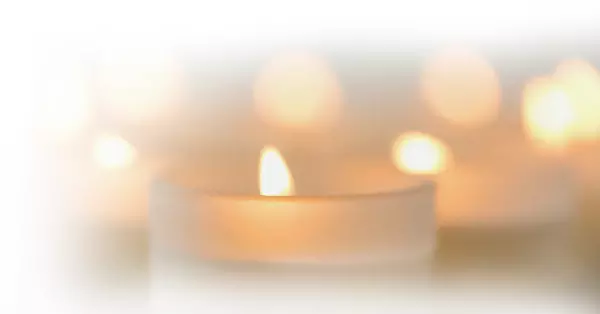 white glass candles burning on a white background with a soft glow of amber light
